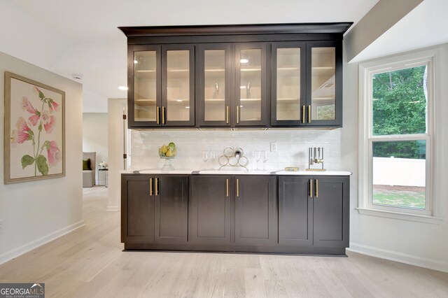 bar with baseboards, decorative backsplash, and light wood-style flooring
