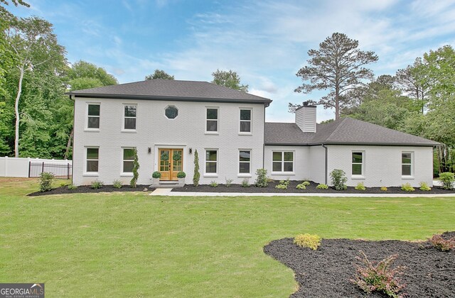 colonial inspired home with fence, french doors, a front yard, and a chimney
