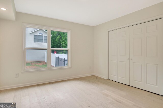 unfurnished bedroom with baseboards, light wood-style flooring, and a closet