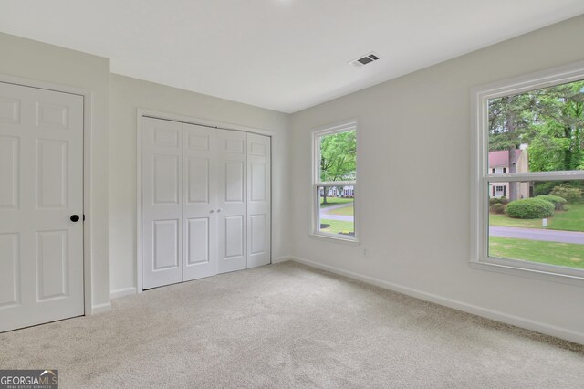 unfurnished bedroom with baseboards, multiple windows, carpet, and visible vents