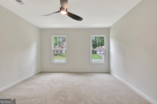 spare room with visible vents, a ceiling fan, a wealth of natural light, and light carpet