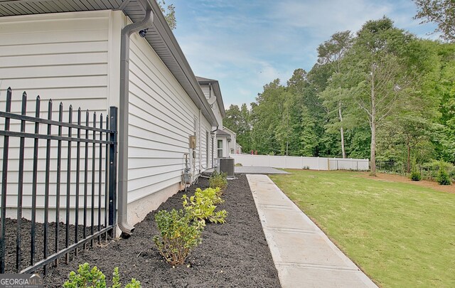 view of side of home featuring central AC, fence, and a yard