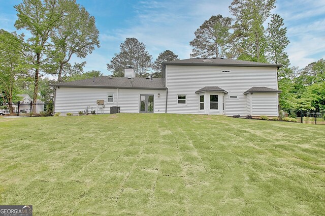 rear view of house featuring a yard, fence, central AC unit, and a chimney