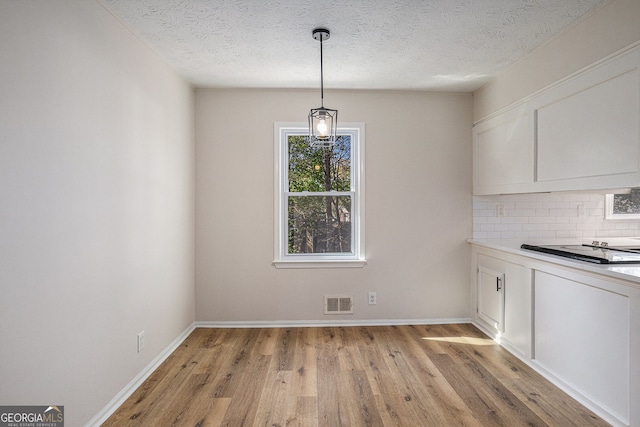 unfurnished dining area with light wood-style floors, baseboards, a textured ceiling, and visible vents