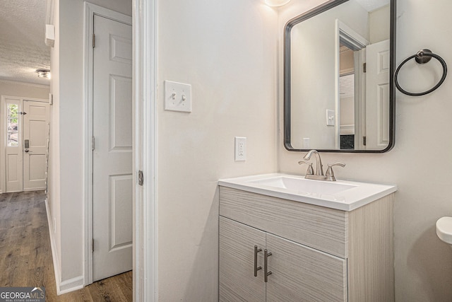 half bathroom with vanity, a textured ceiling, wood finished floors, and toilet
