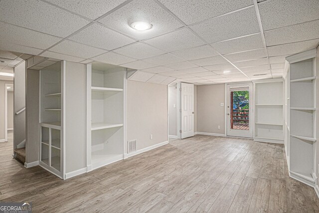 finished below grade area with baseboards, visible vents, a drop ceiling, and wood finished floors