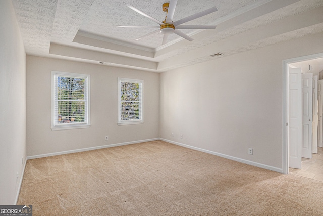 spare room featuring visible vents, baseboards, ceiling fan, light colored carpet, and a tray ceiling