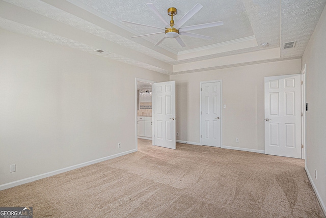 unfurnished bedroom featuring light colored carpet, a textured ceiling, baseboards, a tray ceiling, and visible vents