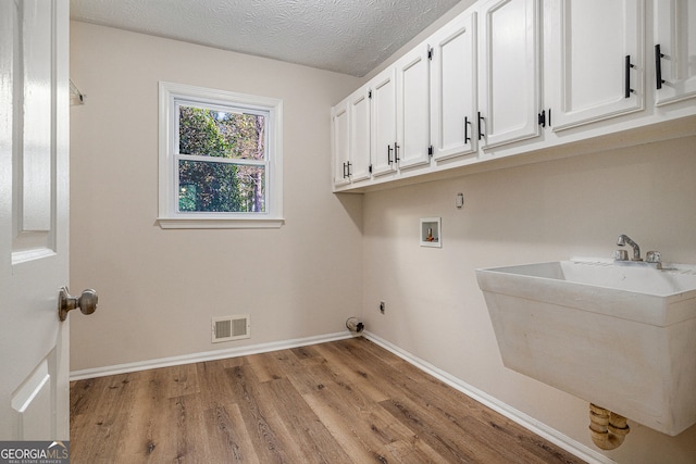 laundry area featuring visible vents, cabinet space, a sink, hookup for a washing machine, and light wood-style flooring