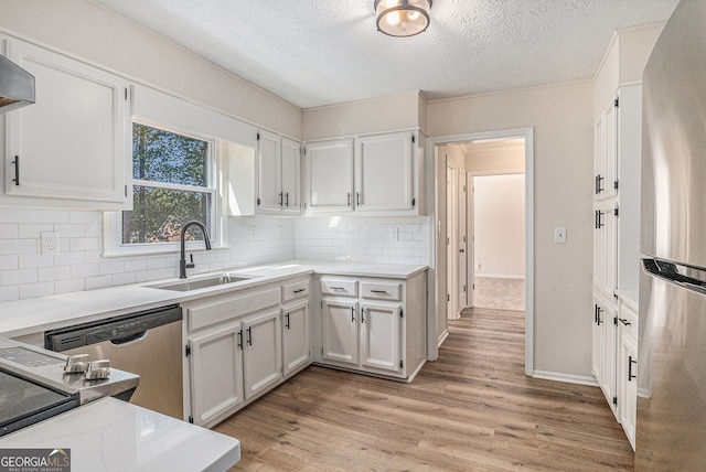 kitchen featuring light wood-style floors, white cabinetry, a sink, backsplash, and stainless steel appliances
