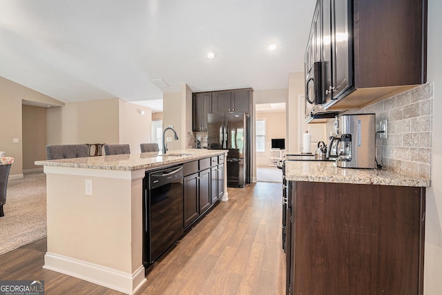 kitchen with freestanding refrigerator, decorative backsplash, dark brown cabinets, black dishwasher, and a sink