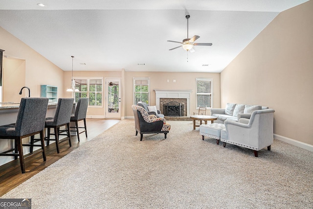 living room with a fireplace with raised hearth, a ceiling fan, baseboards, lofted ceiling, and visible vents