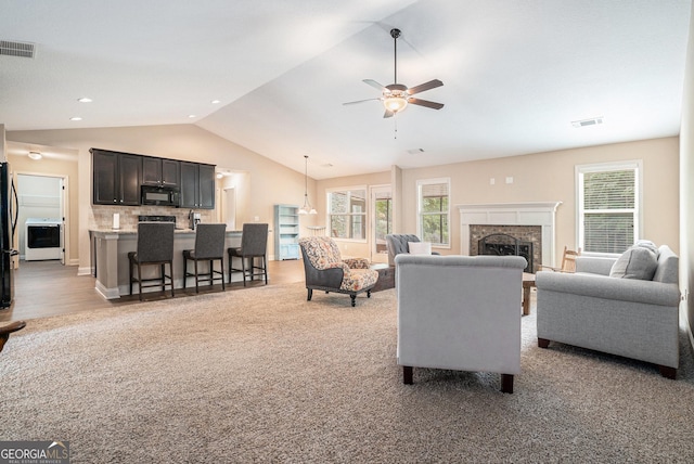 living room featuring visible vents, a fireplace, a ceiling fan, washer / dryer, and vaulted ceiling