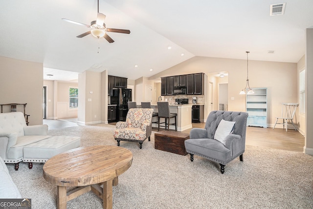 living area featuring ceiling fan, light carpet, high vaulted ceiling, baseboards, and visible vents
