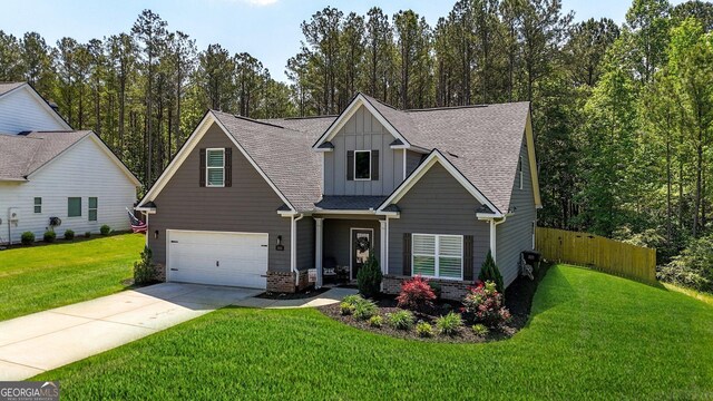 craftsman-style home with board and batten siding, driveway, a front yard, roof with shingles, and an attached garage
