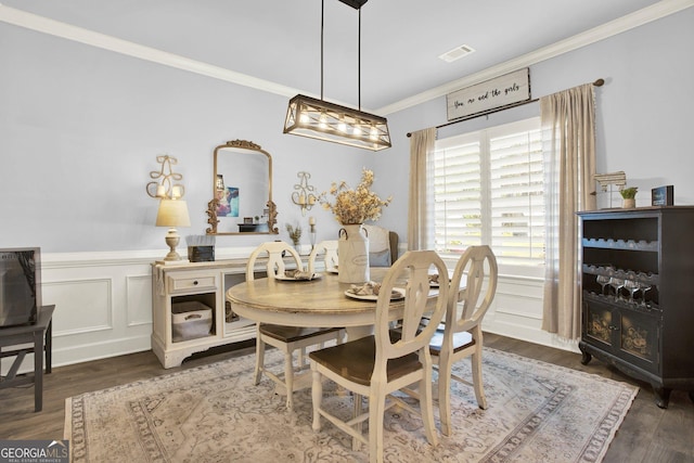 dining room featuring crown molding, visible vents, wainscoting, a decorative wall, and wood finished floors