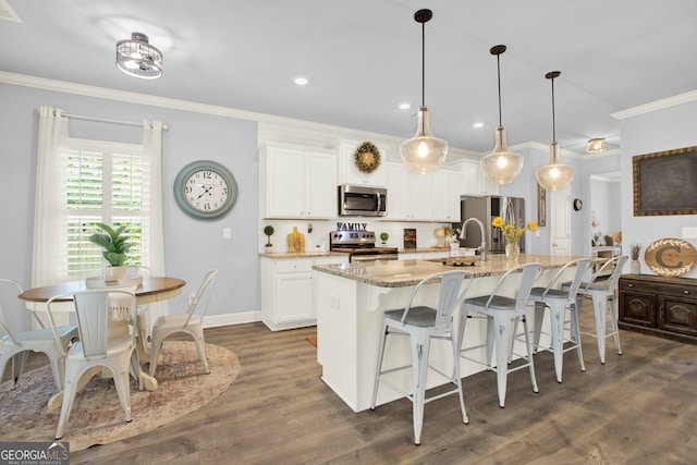 kitchen featuring crown molding, a breakfast bar, an island with sink, white cabinetry, and stainless steel appliances