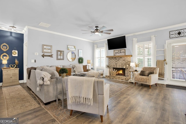 living room featuring a ceiling fan, crown molding, a fireplace, wood finished floors, and baseboards