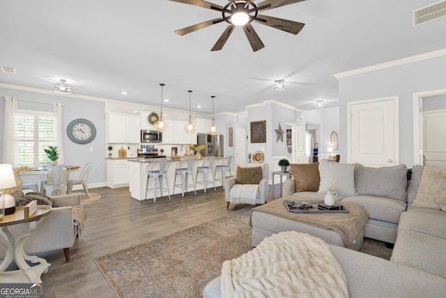 living area with ornamental molding, a ceiling fan, dark wood finished floors, and visible vents