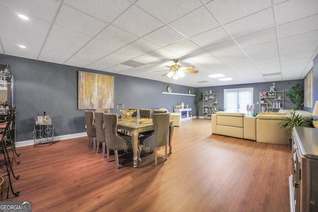 dining area with baseboards, ceiling fan, wood finished floors, and a paneled ceiling