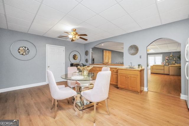 dining space with arched walkways, baseboards, a drop ceiling, and light wood finished floors