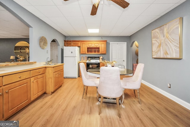 dining room with light wood-style floors, arched walkways, baseboards, and a paneled ceiling