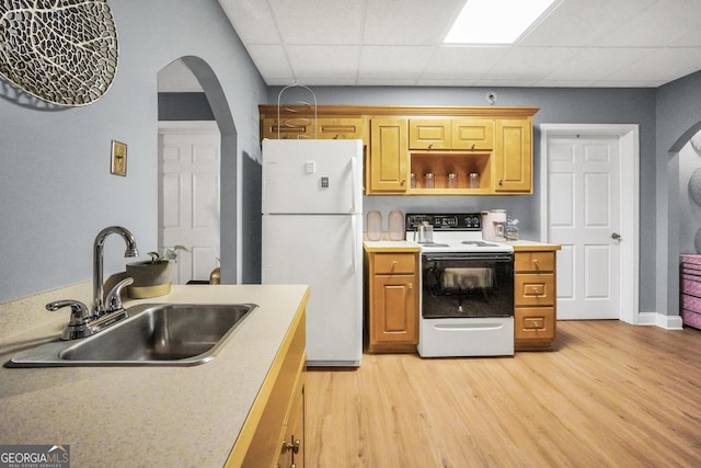 kitchen with a sink, light wood finished floors, arched walkways, and white appliances