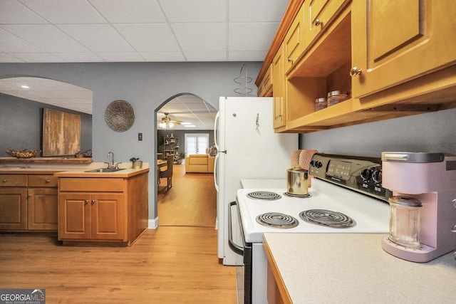 kitchen with a sink, arched walkways, electric range oven, and light wood finished floors
