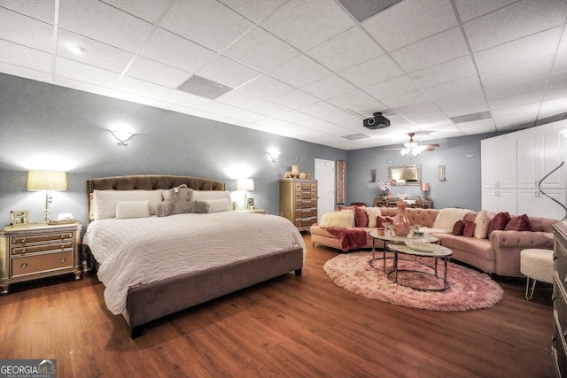 bedroom with ceiling fan, a drop ceiling, and wood finished floors