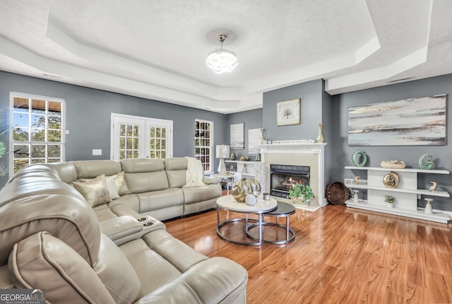 living area featuring a textured ceiling, a fireplace with flush hearth, wood finished floors, and a raised ceiling