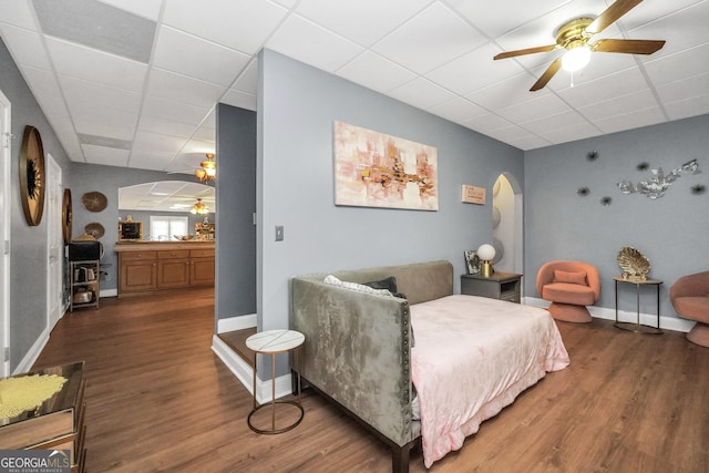 living area with arched walkways, ceiling fan, a drop ceiling, and wood finished floors