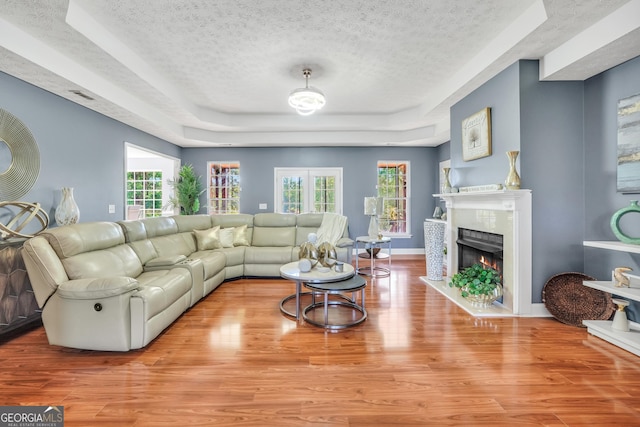 living area featuring a raised ceiling, a textured ceiling, baseboards, wood finished floors, and a lit fireplace