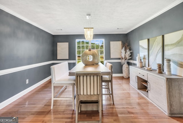 dining space featuring an inviting chandelier, a textured ceiling, light wood-style flooring, baseboards, and ornamental molding