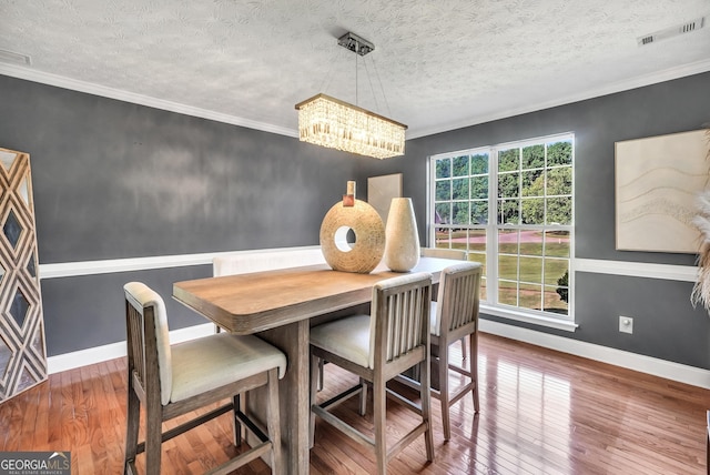 dining space with a textured ceiling, visible vents, hardwood / wood-style flooring, baseboards, and a notable chandelier