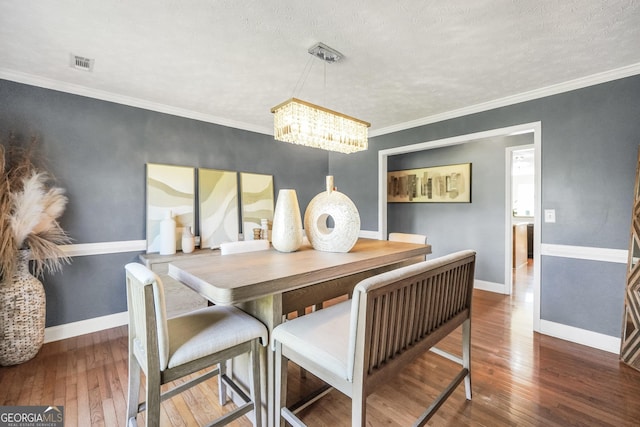 dining room featuring wood-type flooring, a chandelier, baseboards, visible vents, and ornamental molding