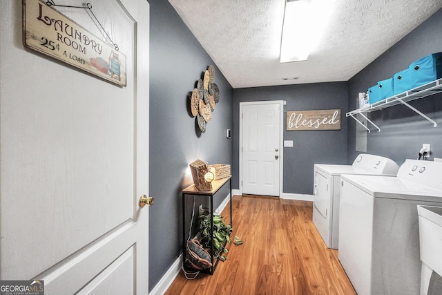 laundry area featuring laundry area, baseboards, light wood-style floors, a textured ceiling, and separate washer and dryer
