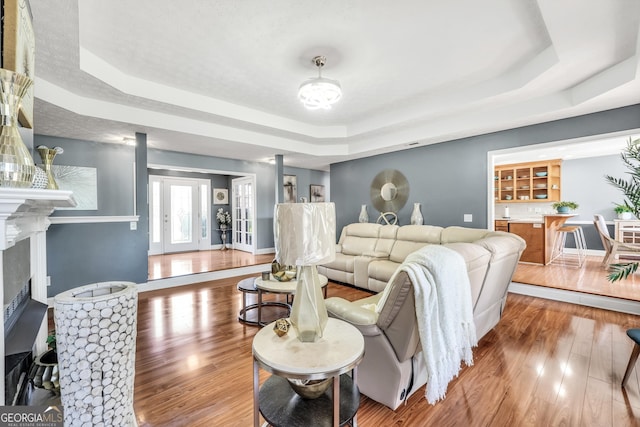living room with a high end fireplace, baseboards, a tray ceiling, and wood finished floors