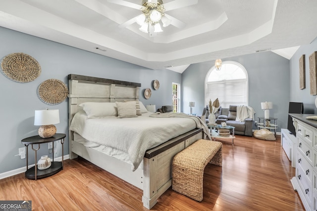 bedroom featuring ceiling fan, visible vents, wood finished floors, a raised ceiling, and baseboards
