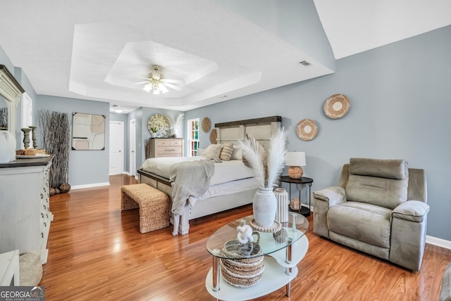 bedroom featuring a ceiling fan, baseboards, wood finished floors, and a raised ceiling