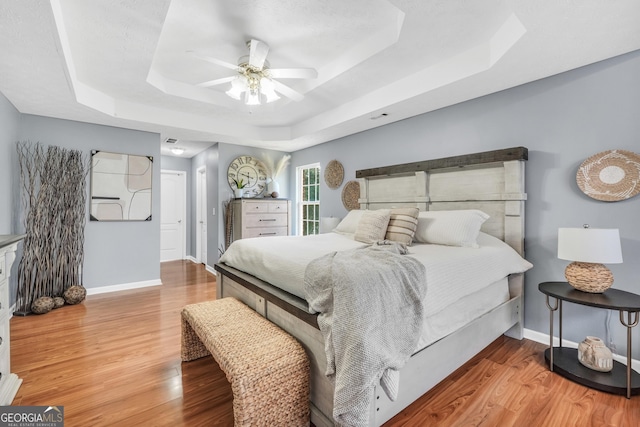 bedroom with a raised ceiling, baseboards, a ceiling fan, and wood finished floors