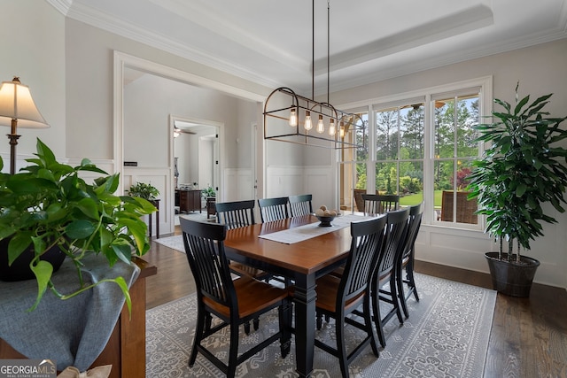 dining area featuring a tray ceiling, wood finished floors, a decorative wall, ornamental molding, and a wainscoted wall