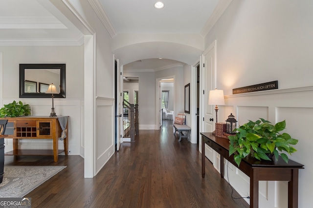 corridor featuring arched walkways, dark wood-type flooring, a decorative wall, ornamental molding, and a wainscoted wall