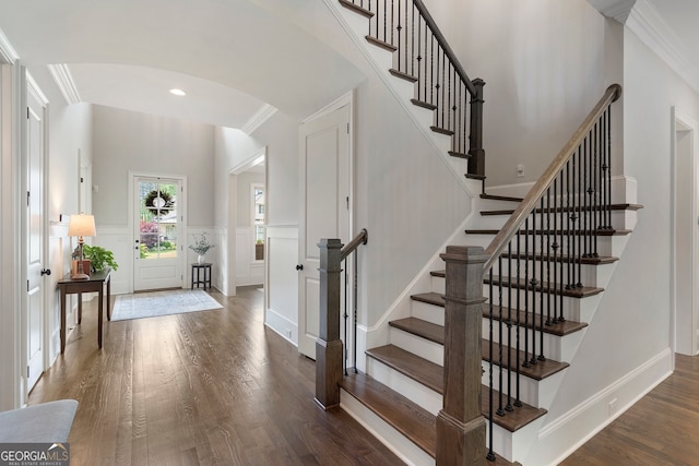 entrance foyer with arched walkways, a decorative wall, stairway, wood finished floors, and ornamental molding