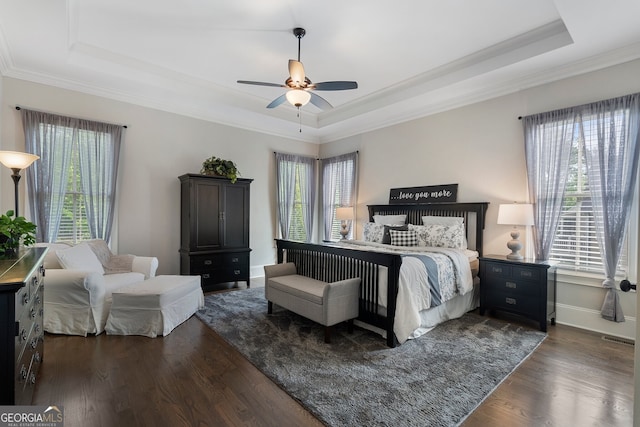 bedroom featuring a tray ceiling, crown molding, dark wood finished floors, a ceiling fan, and baseboards