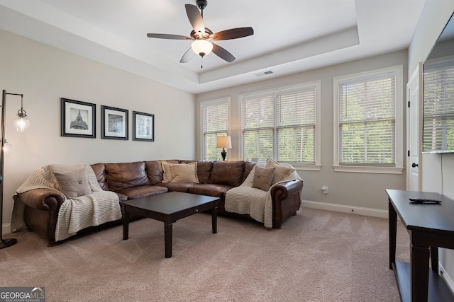 living room featuring light carpet, a ceiling fan, a raised ceiling, and baseboards