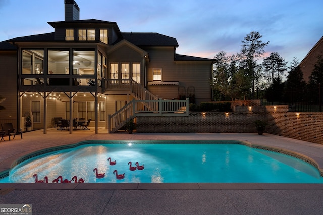 pool at dusk featuring stairway, a patio area, a fenced backyard, and a sunroom
