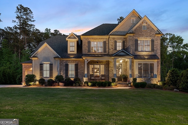 craftsman-style house featuring a lawn, brick siding, a porch, and a standing seam roof