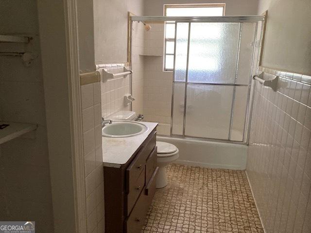 218 Lassiter Dr, Dublin, GA 31021 - full bathroom featuring tile walls, bath / shower combo with glass door, vanity, and toilet