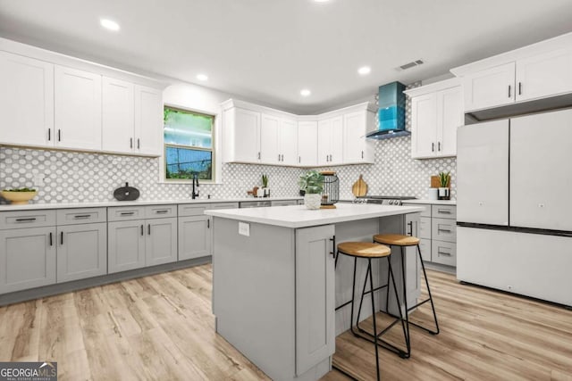 kitchen featuring light countertops, wall chimney exhaust hood, freestanding refrigerator, a kitchen bar, and visible vents