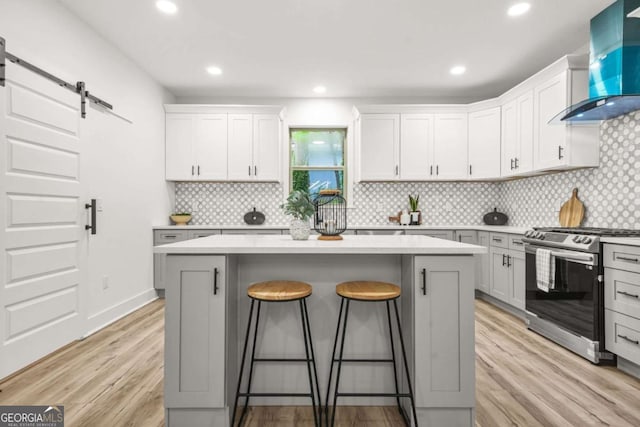 kitchen featuring a kitchen bar, a center island, stainless steel gas range oven, a barn door, and wall chimney exhaust hood